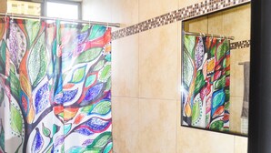 Une salle de bain avec un rideau de douche coloré, des toilettes blanches, un lavabo et un mur carrelé.
