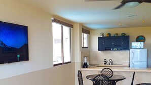 Une cuisine moderne avec un coin repas, un grand téléviseur à écran plat fixé au mur et un ventilateur de plafond.