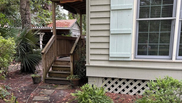 A house with a wooden porch, a staircase, and a garden with various plants and a pathway. - Peace Like A River is a charming one room efficiency,  private entrance. (Bluffton)