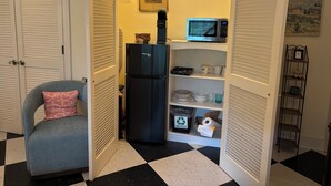 A compact kitchen with a black refrigerator, a microwave, and a small shelf with dishes and a recycling bin. - Peace Like A River is a charming one room efficiency,  private entrance. (Bluffton)