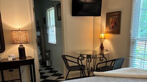 A hotel room with a bed, a desk with a lamp, a TV, and a dining area with chairs and a table. - Peace Like A River is a charming one room efficiency,  private entrance. (Bluffton)