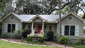 A two-story house with a front porch, a red door, and a small front yard with a pathway and potted plants. - Peace Like A River is a charming one room efficiency,  private entrance. (Bluffton)