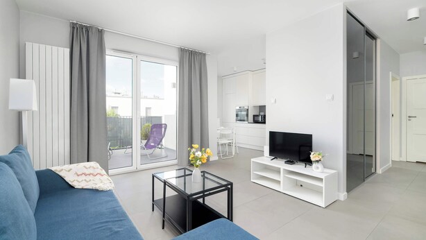 A modern living room with a blue sofa, a glass coffee table, and a flat-screen TV.