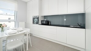 A modern kitchen with white cabinetry, a black countertop, and a dining area with white chairs and a table set for four.