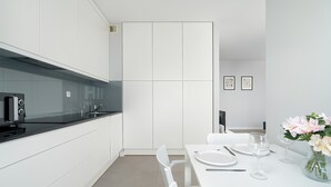 A modern kitchen with white cabinetry, a black countertop, and a dining area with white chairs and a table set for two.