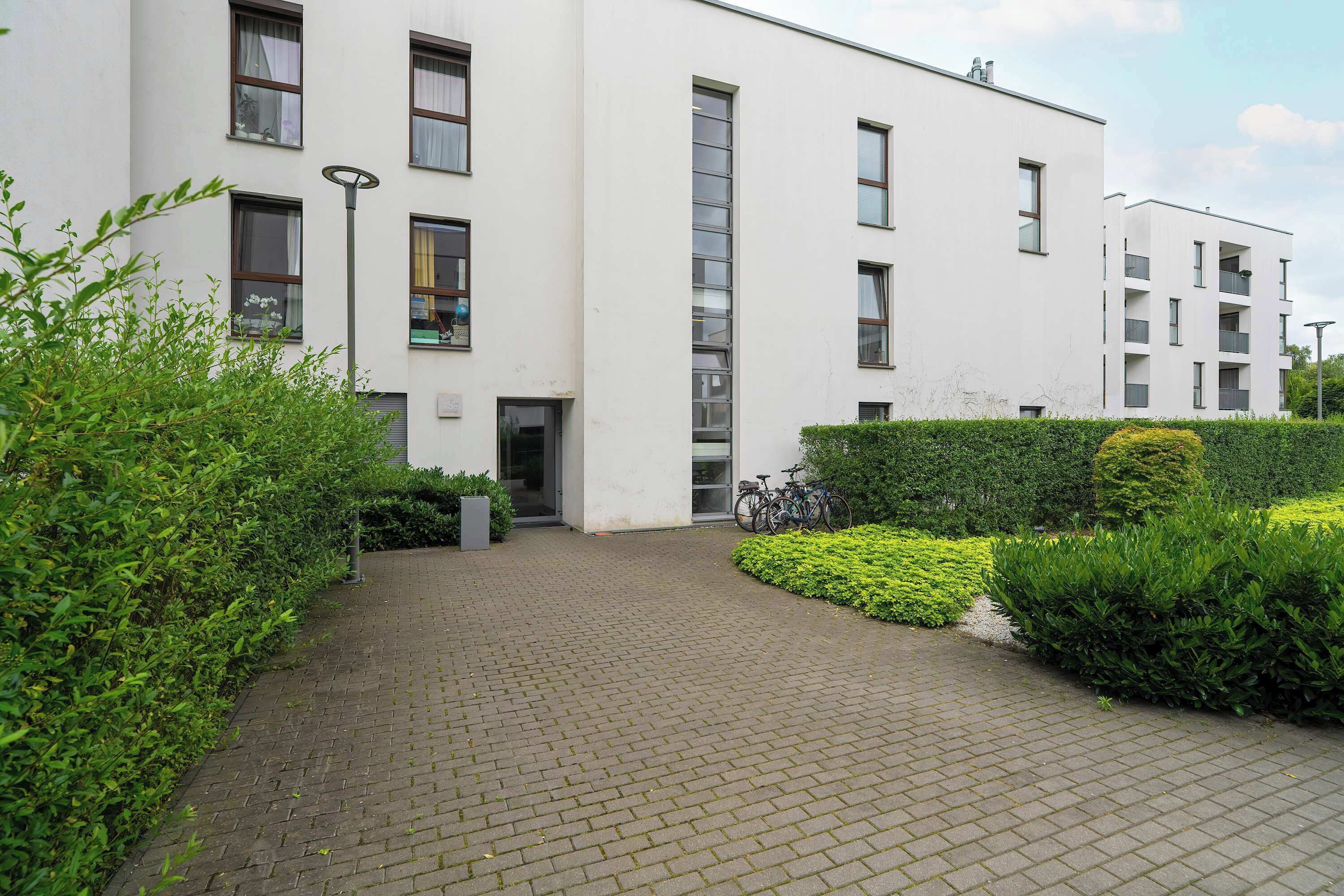 A modern building with a brick pathway, surrounded by well-maintained greenery and a bicycle parked near the entrance.