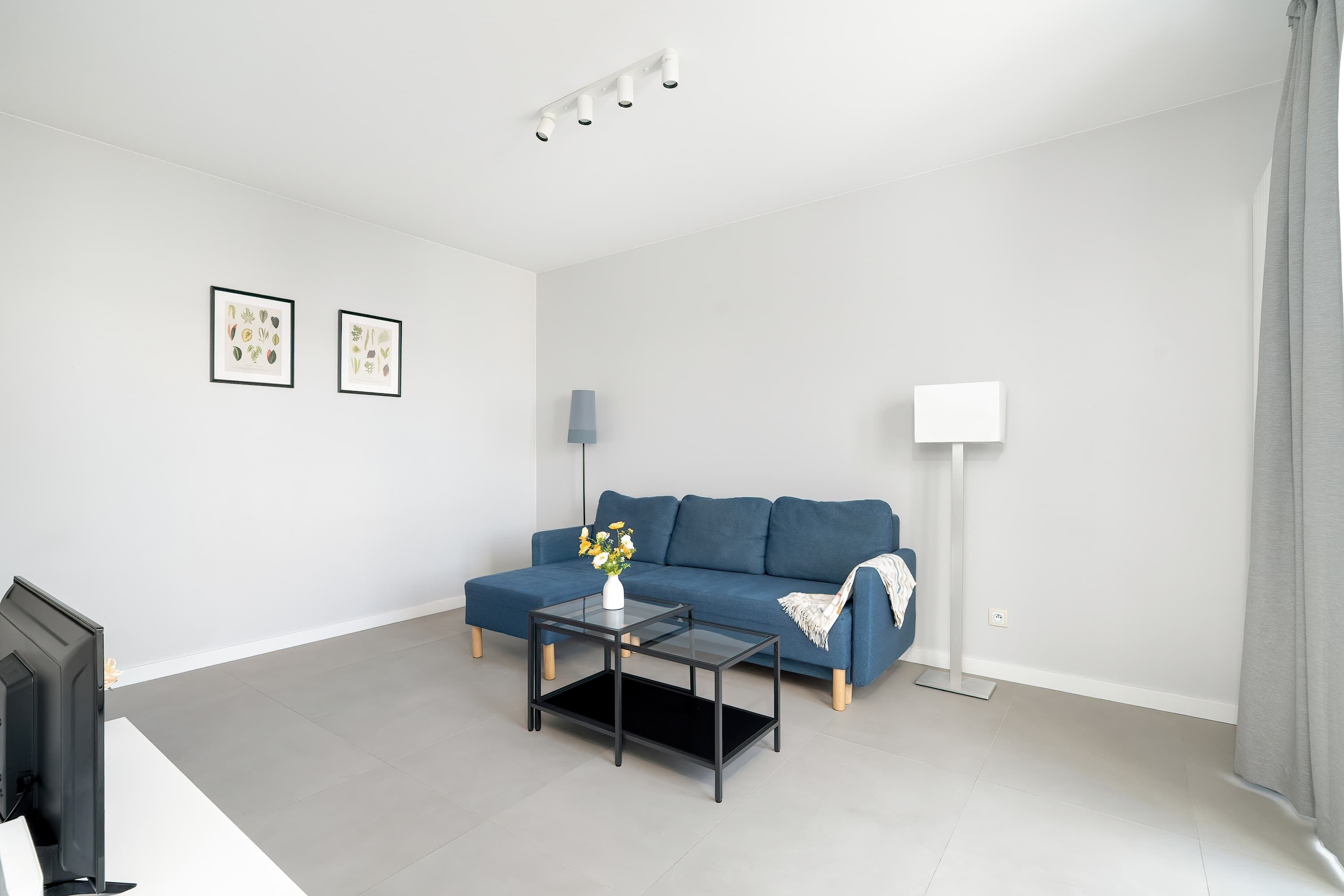 A modern living room with a blue sofa, coffee table, and minimalistic décor in neutral tones.