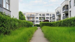 A pathway flanked by lush green hedges leading to modern apartment buildings with balconies and outdoor plants.