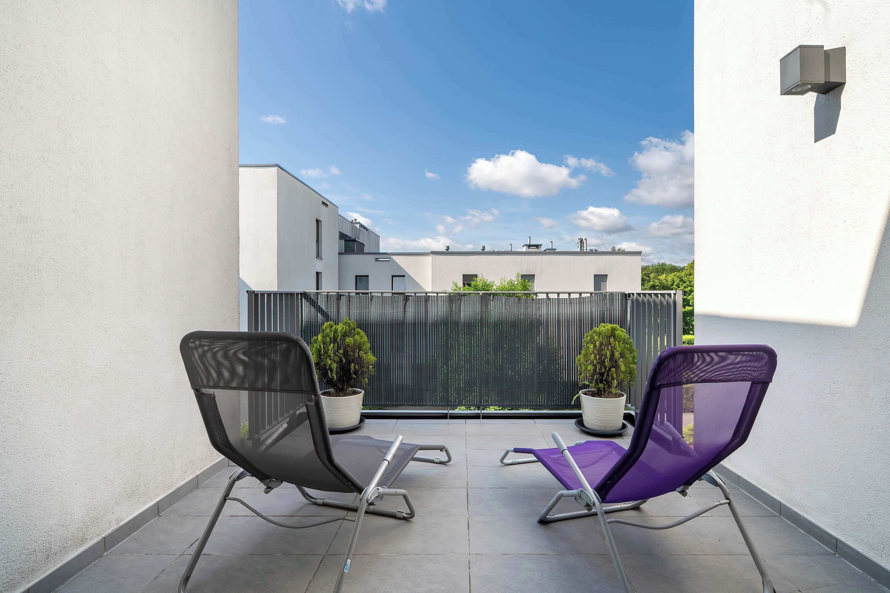 Un balcon avec deux fauteuils de jardin, un pot de fleurs et une vue sur les immeubles.