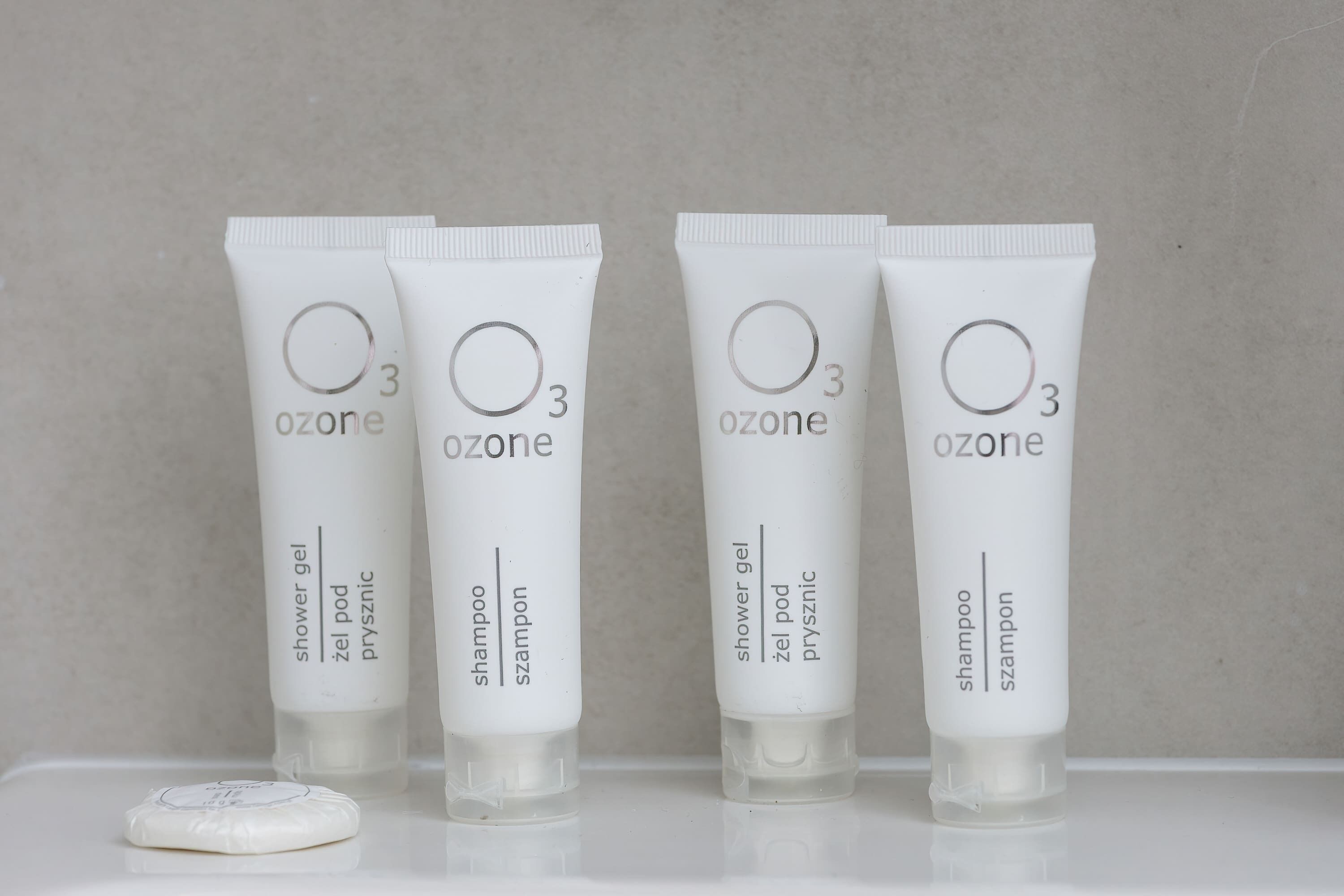 Cuatro tubos blancos de gel de ducha y champú Ozone sobre una superficie blanca.