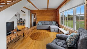 Ein geräumiges Wohnzimmer mit grauem Ecksofa, Holzböden, einem Fernseher und einem Essbereich mit Stühlen und einem Tisch.