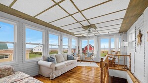 Ein geräumiges Zimmer mit Holzboden, weißen Wänden und großen Fenstern mit Blick nach draußen.