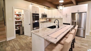 Una cocina con armarios blancos, electrodomésticos de acero inoxidable, encimera de mármol y techo de madera.