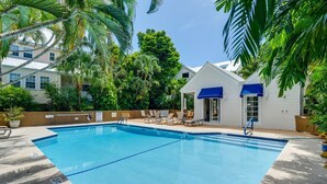 A swimming pool with lounge chairs and a small building with blue awnings. - Your Breezy Old Town Retreat Awaits (Key West)