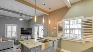 A modern kitchen with granite countertops, a stainless steel sink, and a built-in dishwasher. There are pendant lights above the island, and the room has a gray and white color scheme. - Your Breezy Old Town Retreat Awaits (Key West)