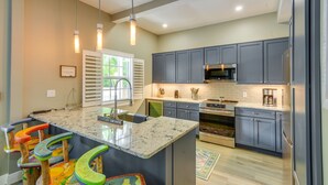 A modern kitchen with grey cabinets, a large island with colorful stools, stainless steel appliances, and pendant lighting. - Your Breezy Old Town Retreat Awaits (Key West)