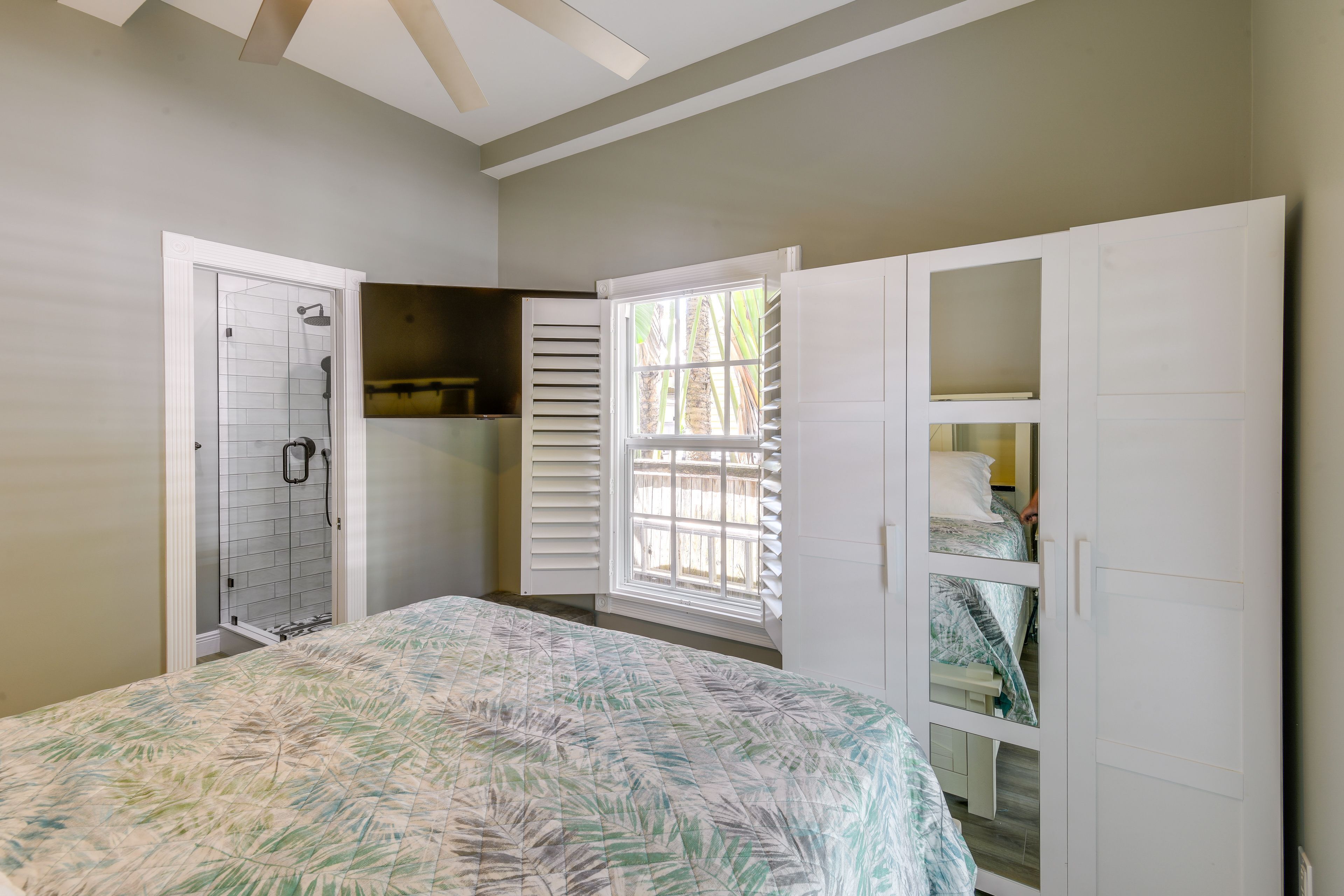 A bedroom with a bed, a walk-in closet, a window with shutters, and a shower area.