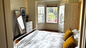 Une chambre à coucher comprenant un lit, une commode, un miroir et une fenêtre donnant sur un paysage verdoyant.