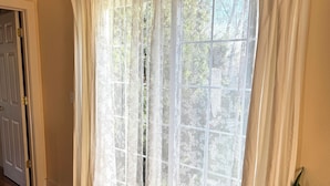 Une pièce dotée d’une grande fenêtre ornée de rideaux blancs et légers, d’un plancher en bois et d’une plante en pot.