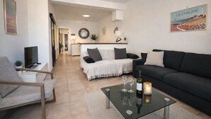 Una sala de estar moderna con sofá, sillón y una mesita de centro. Hay un televisor, un espejo y un cuadro en la pared.