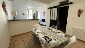Un comedor con una mesa lista para cuatro, una cocina al fondo y un divisor corredizo que da a otra habitación.