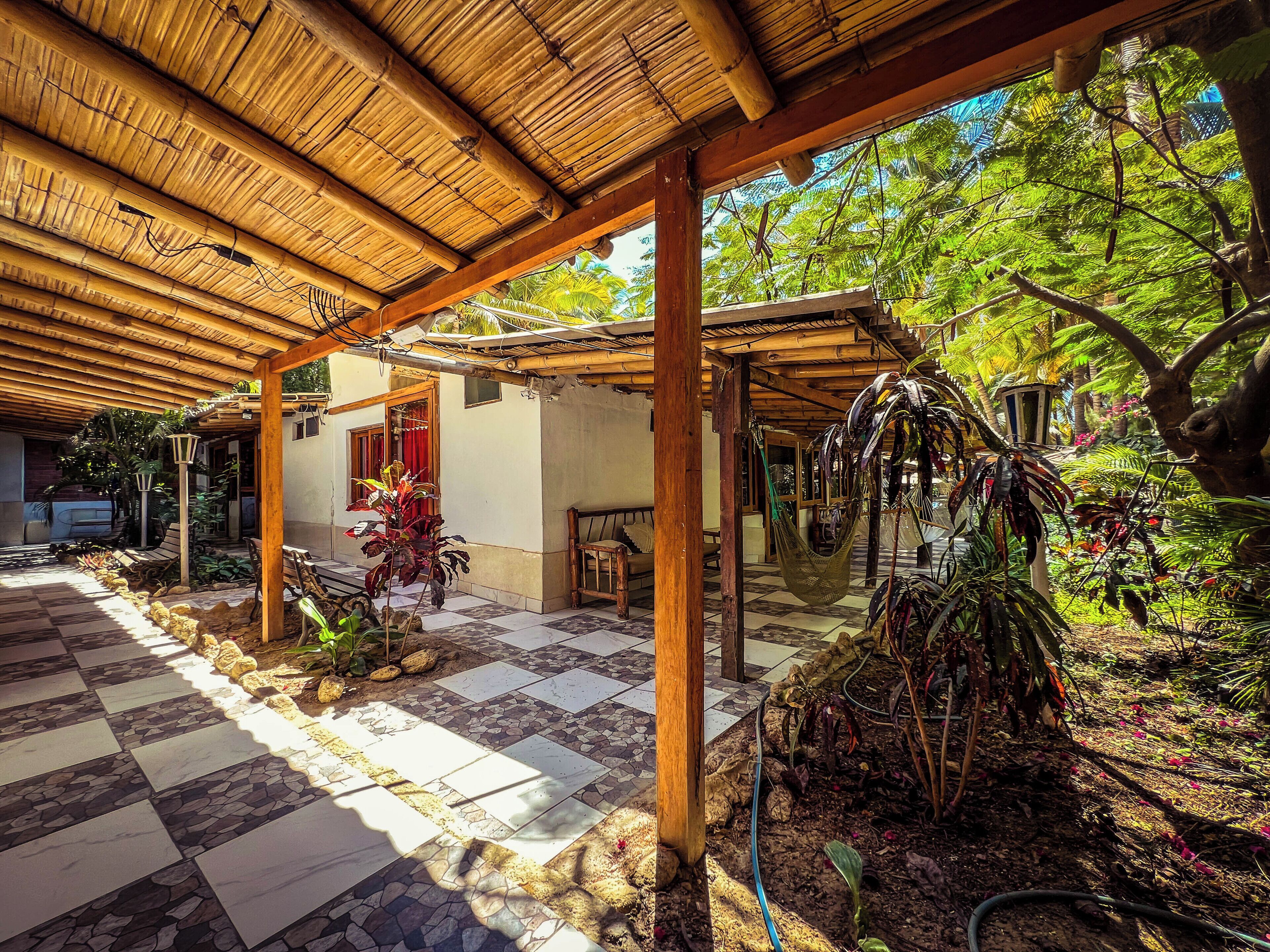 Un espacio al aire libre techado con piso a cuadros, vigas de madera y plantas tropicales.