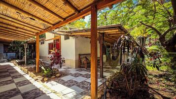 Un espacio al aire libre techado con piso a cuadros, vigas de madera y plantas tropicales.