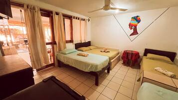 A room with two beds, a ceiling fan, a window with curtains, and a wall with a picture.