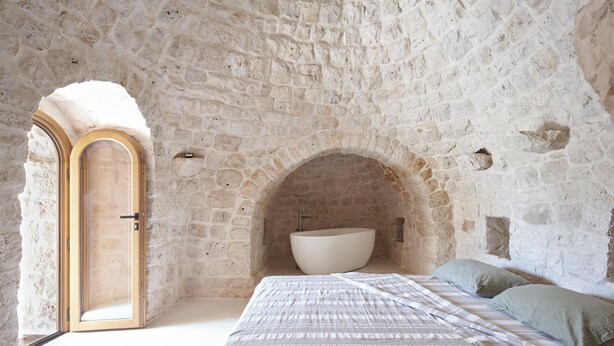Une chambre aux murs de pierre, avec un lit, une baignoire et une porte.