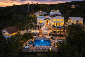 A multi-story house with a swimming pool, outdoor seating, and a landscaped garden. - Luxe Hillside Home w/ Pool, Spa, Game Room & Views (Wimberley)