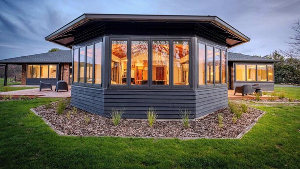 Ett modernt hus med en stor glasveranda, en täckt uteplats och en välskött gräsmatta.