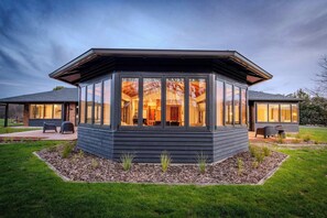 A modern house with a large glass enclosure, a covered patio, and a well-maintained lawn.
