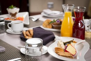 Desayuno con un plato de comida, un vaso de agua, una taza de café y dos botellas de jugo.