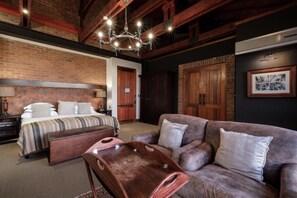 Une chambre d’hôtel avec un grand lit, un canapé, une table d’appoint en bois et un lustre.