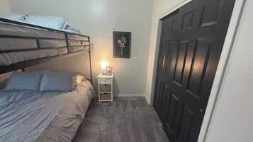 A bedroom with a bunk bed, a bedside table with a lamp, a framed picture on the wall, and a dark door.