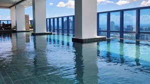 An indoor infinity pool with clear blue water, large windows, and a view of the city skyline. - Virgo Nest Rentals - 38th Park Ave, IT Park Cebu - City View (Cebu City)