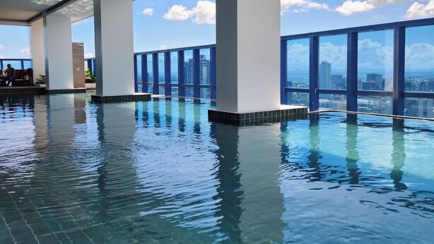 An indoor infinity pool with clear blue water, large windows, and a view of the city skyline. - Virgo Nest Rentals - 38th Park Ave, IT Park Cebu - City View (Cebu City)