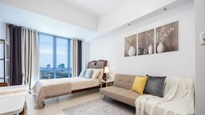 A modern bedroom with a bed, sofa, and a city view through large windows. - Virgo Nest Rentals - 38th Park Ave, IT Park Cebu - City View (Cebu City)