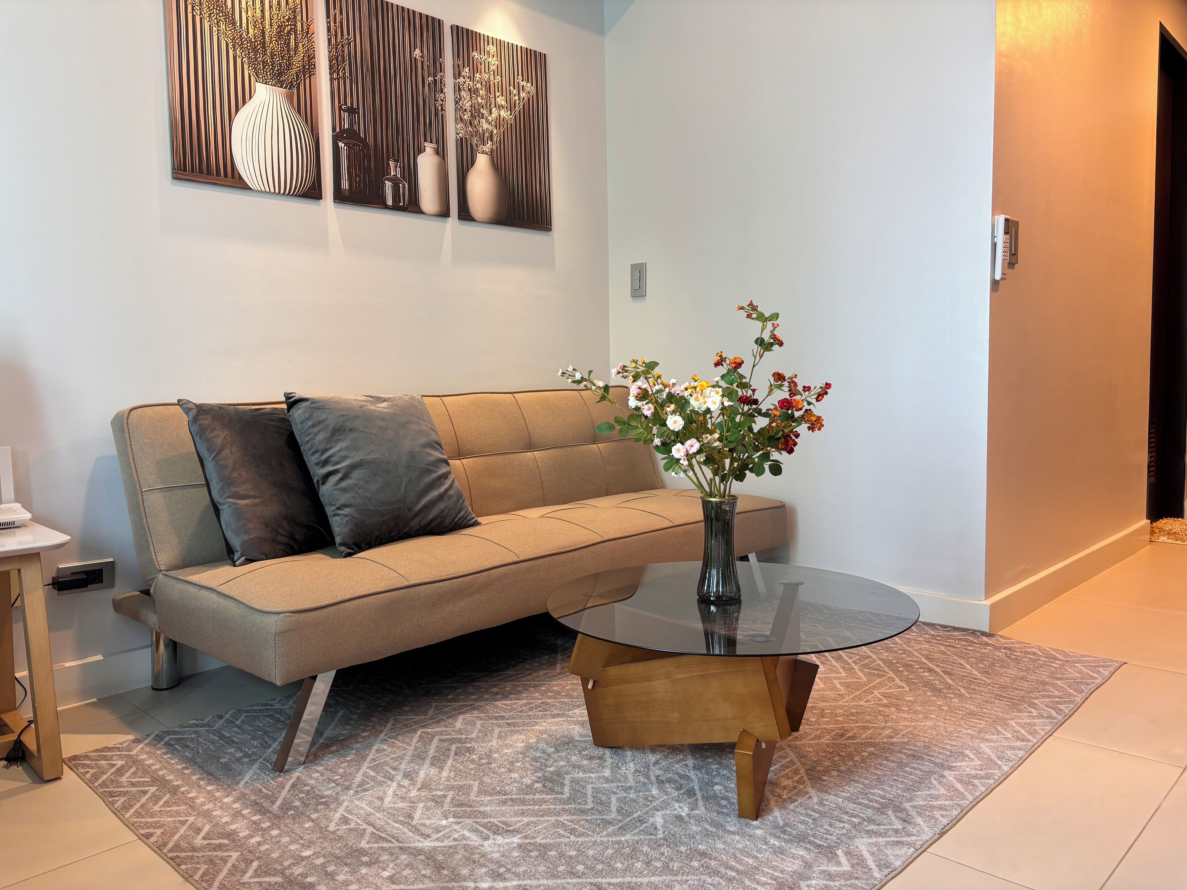 A modern living room with a beige sofa, a glass coffee table, and a vase with flowers.
