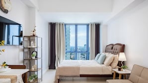 A modern bedroom with a large window, a bed, a sofa, a side table, a bookshelf, and a clock on the wall. - Virgo Nest Rentals - 38th Park Ave, IT Park Cebu - City View (Cebu City)