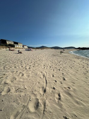 A sandy beach with footprints, a few people, and buildings in the background.