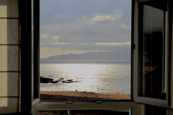 A view from a window overlooking a calm sea with distant mountains.