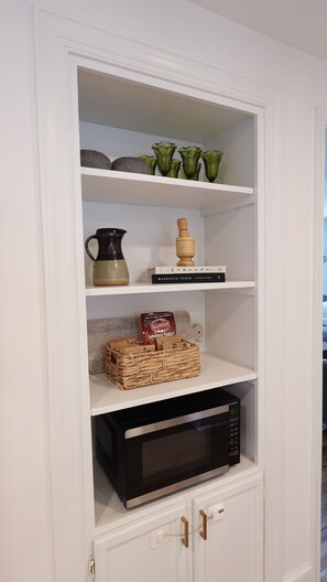 A white cabinet with shelves containing kitchenware, a book, and a microwave. - Cozy 3BR Retreat w/ Patio, Fire Pit & Yard (Winchester)
