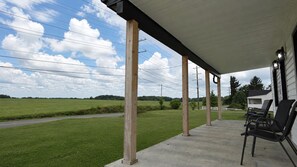 A covered outdoor area with a concrete floor, wooden posts, and a white building in the background. - Cozy 3BR Retreat w/ Patio, Fire Pit & Yard (Winchester)