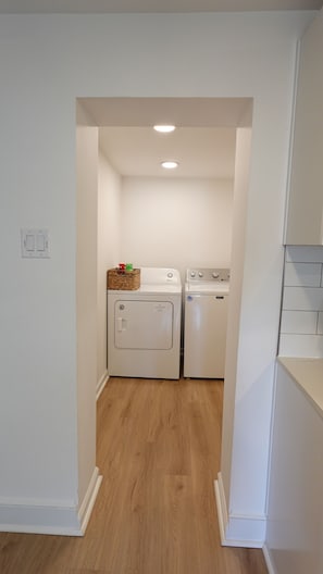 A laundry room with a washing machine and dryer, wooden flooring, and a ceiling light. - Cozy 3BR Retreat w/ Patio, Fire Pit & Yard (Winchester)