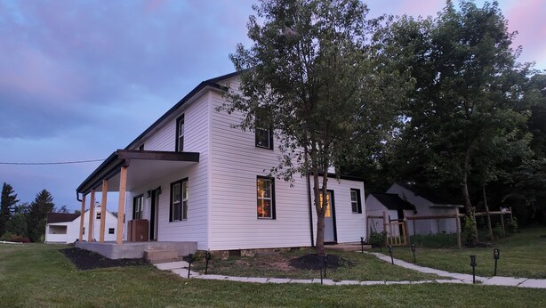 A two-story house with a covered porch, a small front yard, and a tree in front.