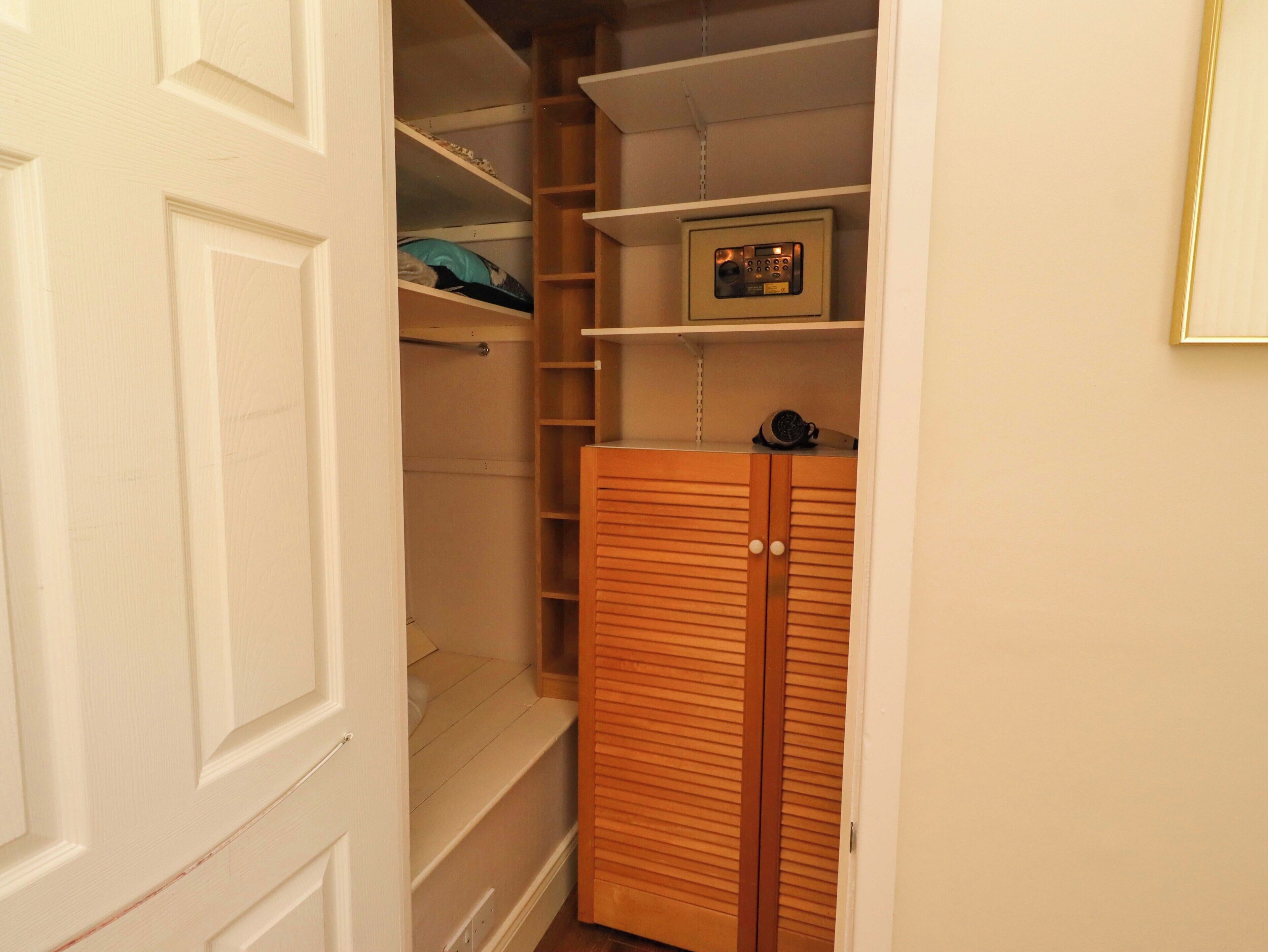 A walk-in closet with wooden doors, shelves, and a small electronic device on the top shelf.