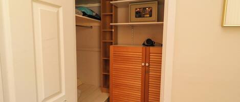 A walk-in closet with wooden doors, shelves, and a small electronic device on the top shelf.