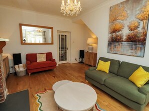 A living room with a red sofa, green sofa, white coffee table, and a chandelier.