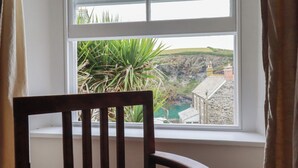A view from a window with a chair in the foreground, overlooking a coastal landscape with buildings and greenery. - 84 Fore Street (Port Isaac)